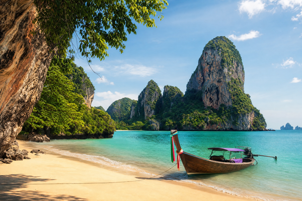 A sun-kissed, palm-lined Krabi beach with clear blue waters under a partly cloudy sky.