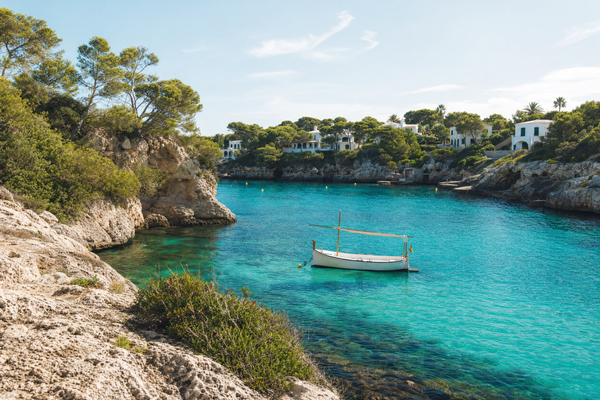 A tranquil beach in Menorca with turquoise water, gentle sunshine and lush greenery.