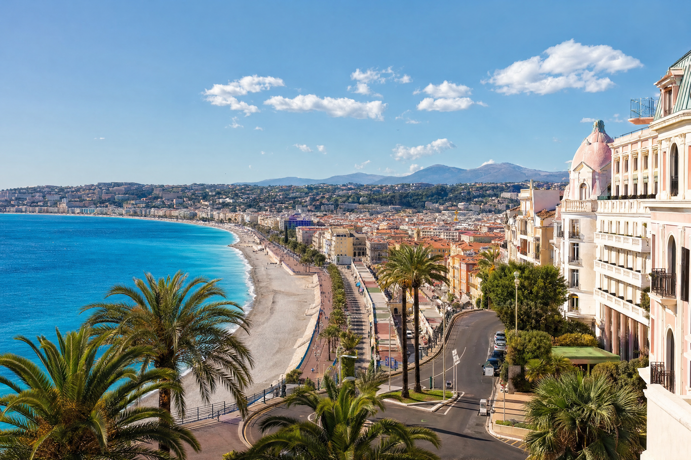 Nice beach with blue sea, sunny sky and people strolling along the Promenade des Anglais