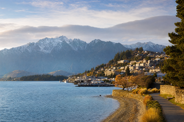 A panoramic view of Queenstown with Lake Wakatipu and surrounding mountains under a bright sky.